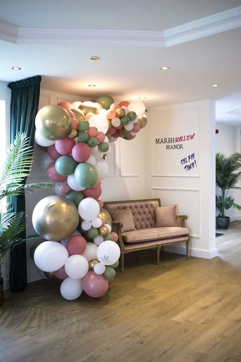 Pastel and gold balloon arch beside a blush velvet bench and Marshmallow Manor wall sign.