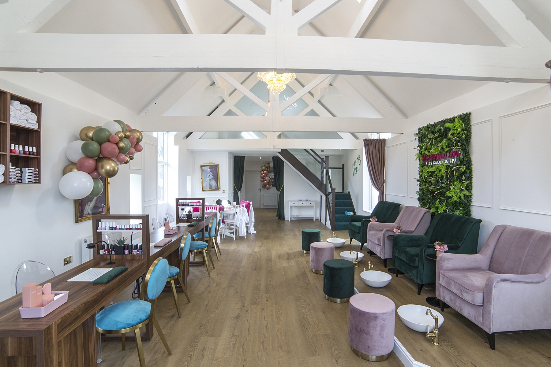 Airy manor lounge with white roof beams, pastel armchairs, a vanity table and a green floral wall.
