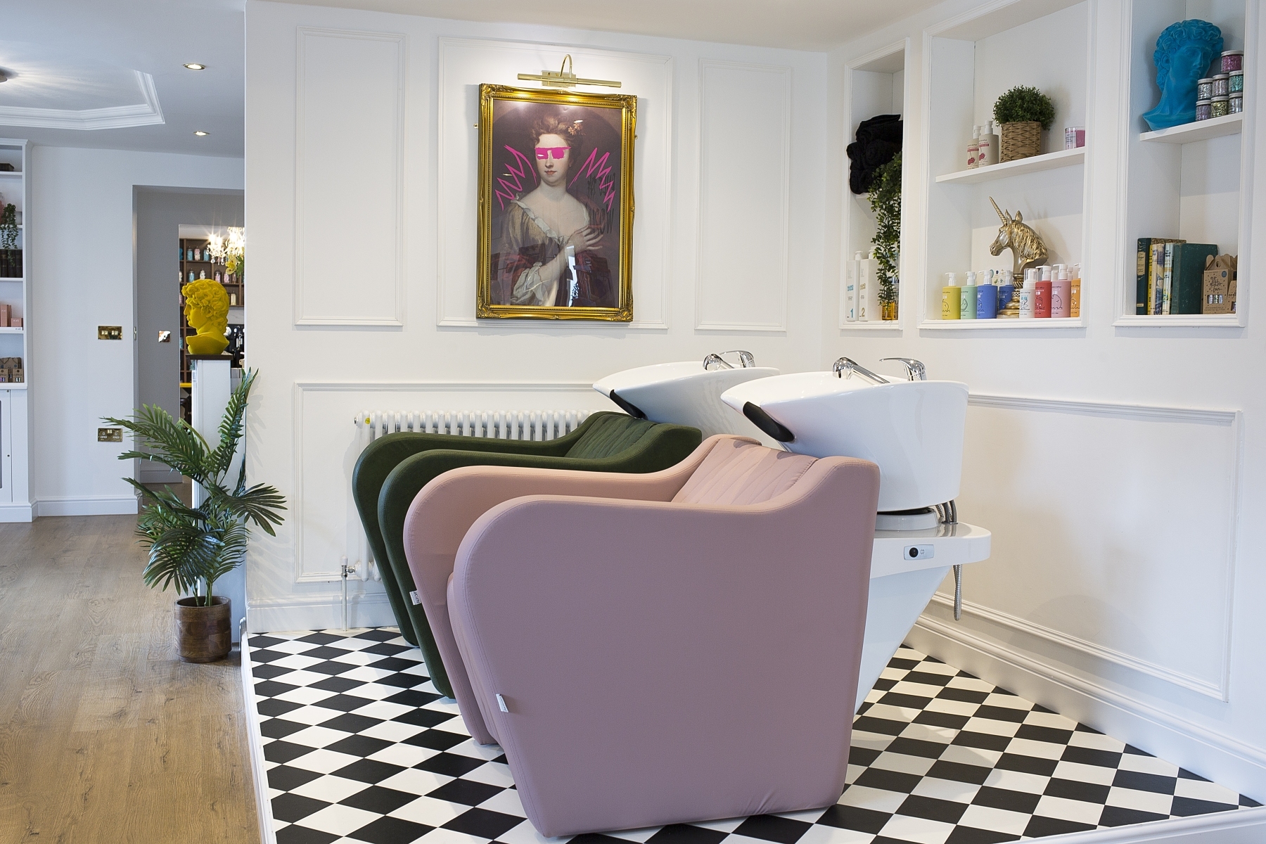 Pastel pink and dark green hair wash chairs with white basins on a black and white tiled floor.