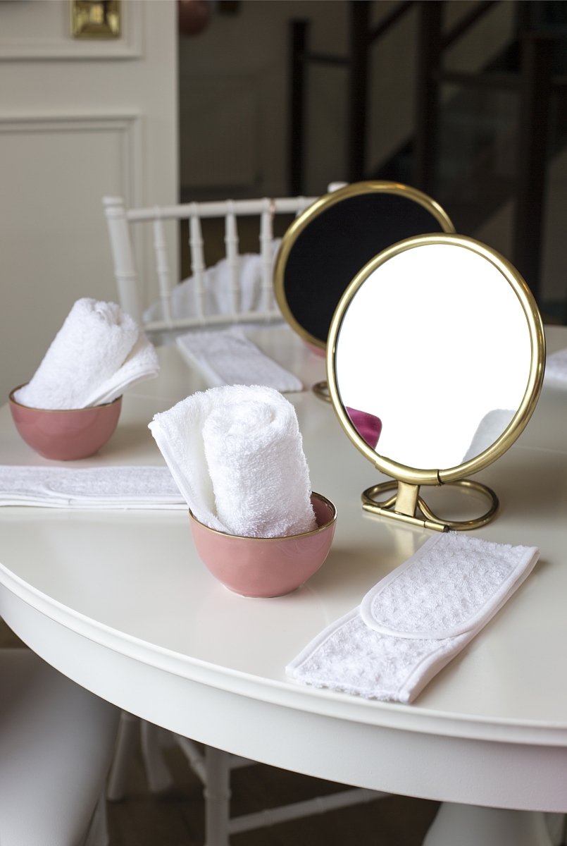 Rolled white spa towels in pink bowls beside a round gold tabletop mirror.